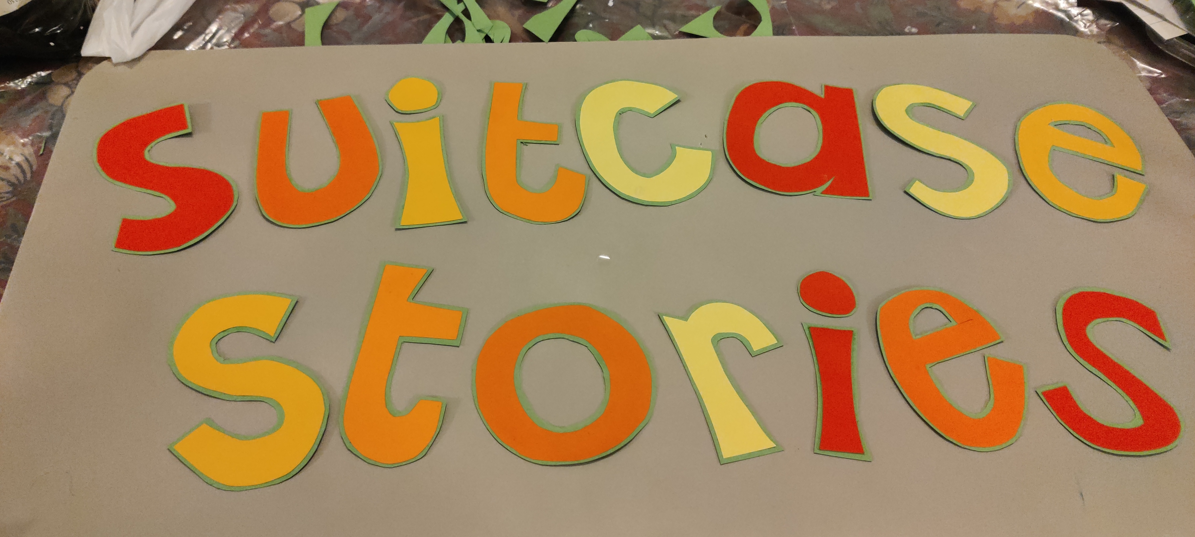words suitcase stories cut out of sugar paper in yellows oranges and reds. 