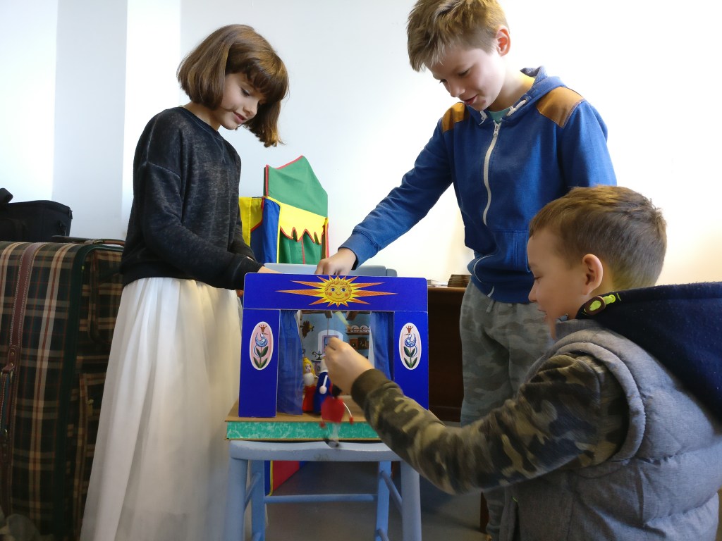 three children are playing with a mini theatre and small puppets