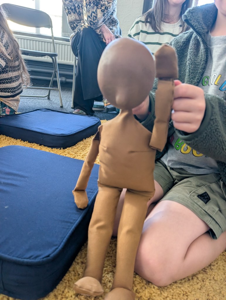 a table top puppet is waving at the camera - a child's hand can be seen manipulating it.