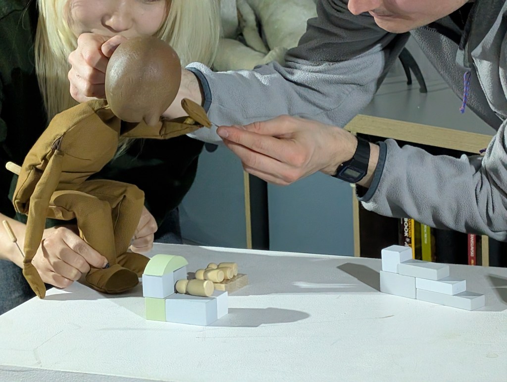 a puppet is examining smaller puppets whilst being manipulated by two puppeteers. 