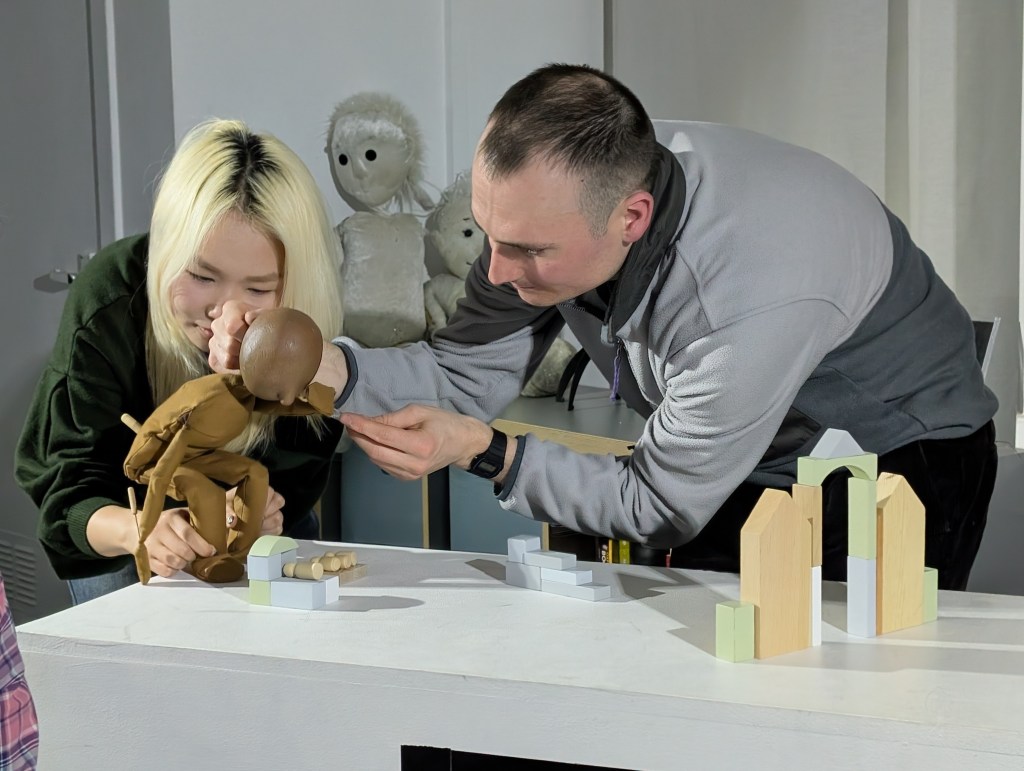 two adult puppeteers are working with a small table top puppet.